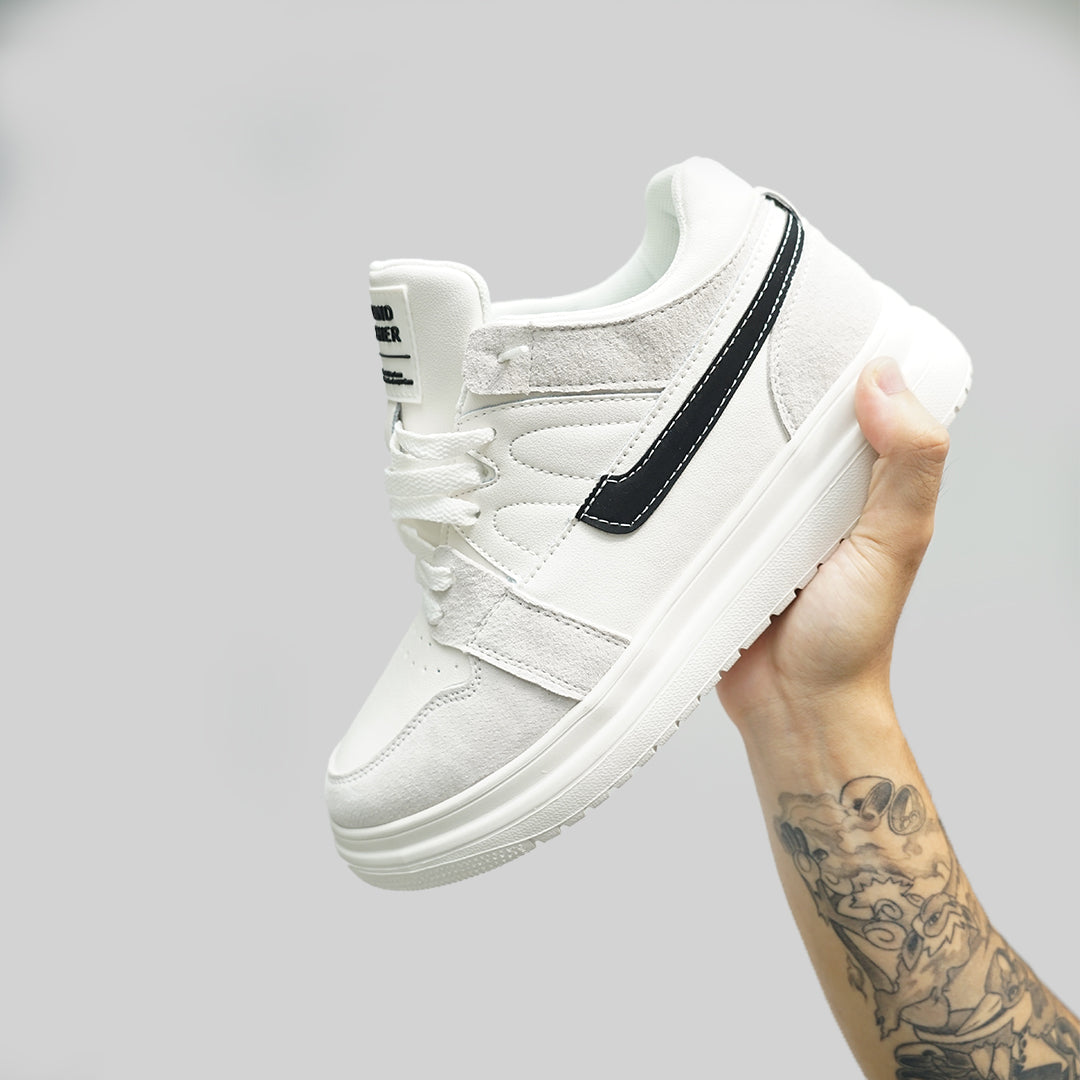 A hand holding a stylish white sneaker with black accents against a gray background, showcasing its sleek design.