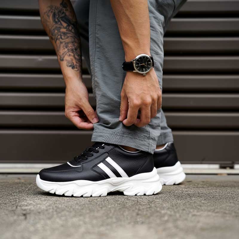 Person wearing black sneakers with white soles, standing on a concrete surface.