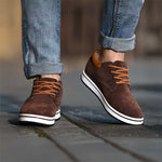 Brown suede shoes with white soles worn with rolled-up jeans on a blurred background