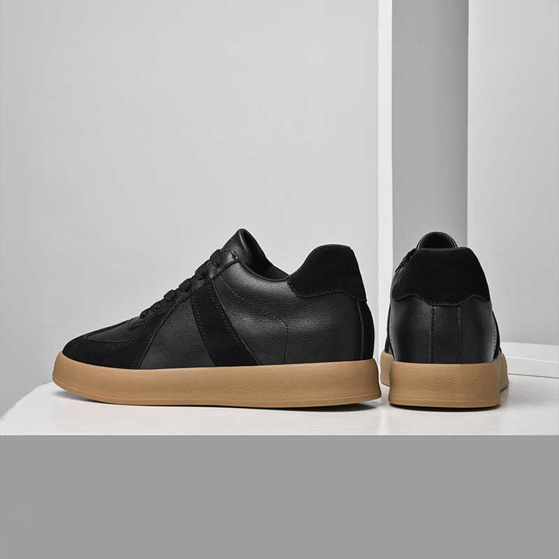 Pair of black sneakers with brown soles on a white surface.