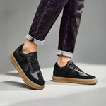 Black sneakers with brown soles worn with dark jeans on a gray background