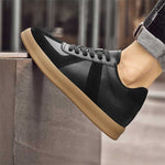 Black sneaker with brown sole worn by a person against a blurred background