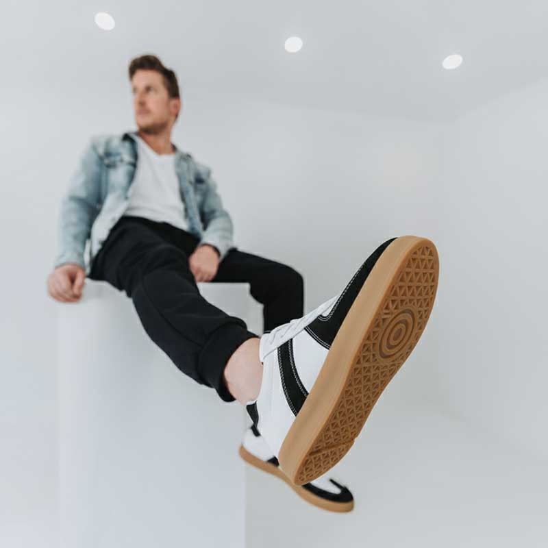 Person wearing a white sneaker with black accents and tan soles on a light gray background
