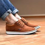Brown suede shoes with white soles worn by a person on a wooden floor.