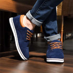 Navy blue sneakers with brown laces worn by a person on a wooden floor.