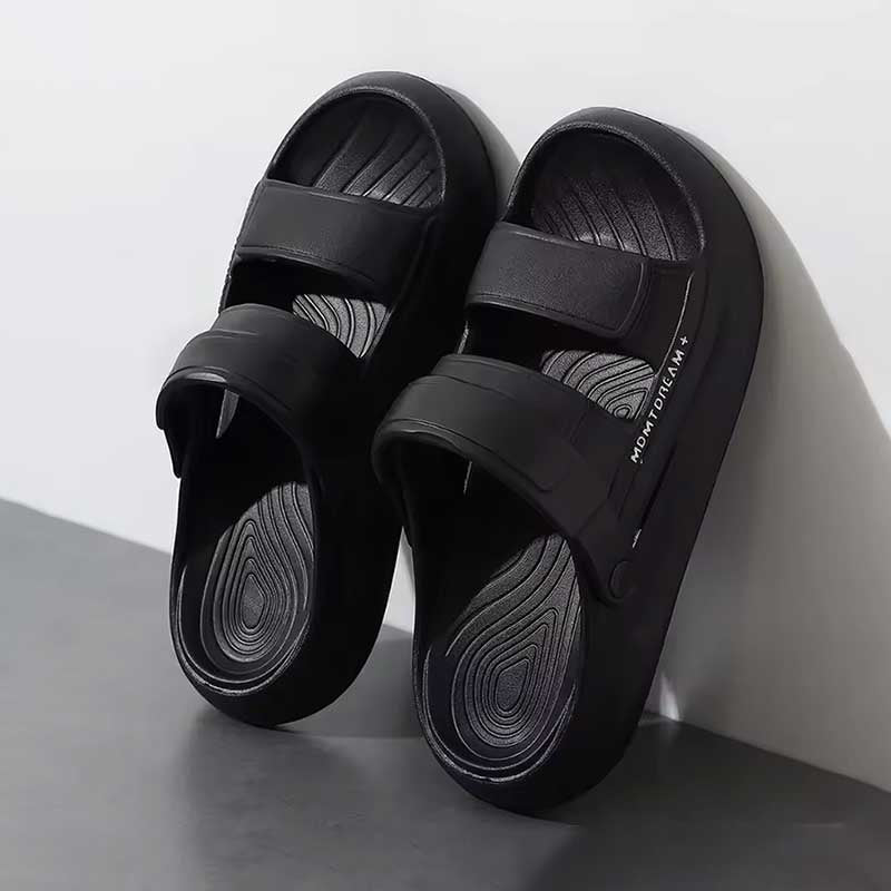 Black sandals resting on a wall on a light gray background