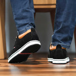 Black shoes with white soles worn by a person on a wooden floor.