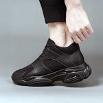 Black height increasing sneaker being worn on a grey background
