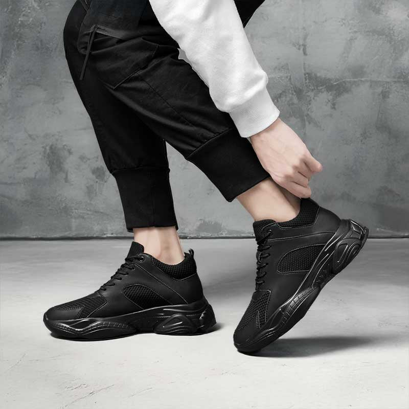 Person wearing black Stratus elevator sneakers on a grey background