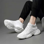 Man sitting in white elevator sneakers worn with black pants on a grey background