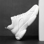 White elevator sneaker leaning against a dark grey wall.