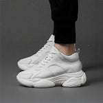 White height boosting sneakers worn with black pants on a grey background