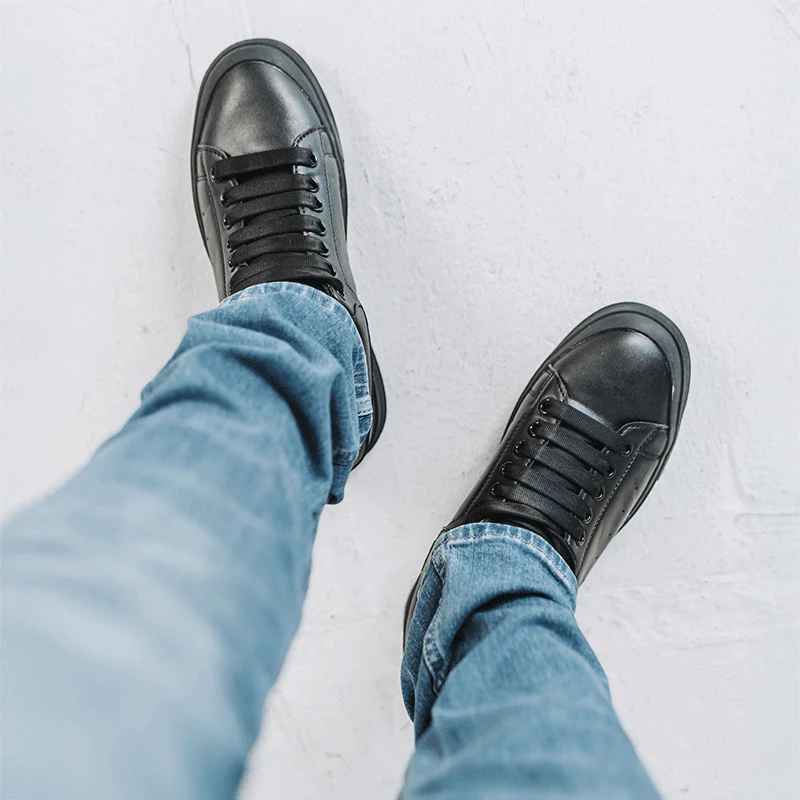 A pair of black sneakers worn with blue jeans, viewed from above on a light textured surface.