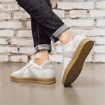 White sneakers with brown soles worn by a person against a brick wall background