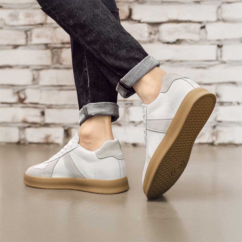 White sneakers with brown soles worn by a person against a brick wall background