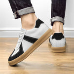 White sneakers with black accents and brown soles worn by a person on a wooden floor.